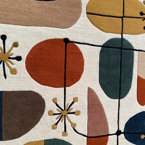 Puede incluir: Primer plano de una colorida alfombra abstracta con un dise&ntilde;o moderno de mediados de siglo. La alfombra presenta varias formas en tonos de azul, marr&oacute;n, naranja, amarillo y rosa sobre un fondo blanco. L&iacute;neas negras conectan las formas, creando un patr&oacute;n &uacute;nico.