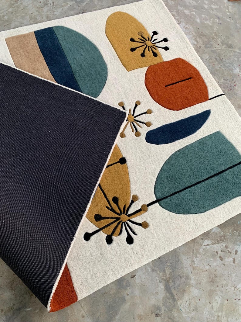 Puede incluir: Una alfombra rectangular con fondo crema y formas abstractas coloridas. El dise&ntilde;o incluye formas en verde azulado, azul marino, naranja y amarillo mostaza, con detalles lineales negros. La parte inferior de la alfombra es azul marino oscuro.
