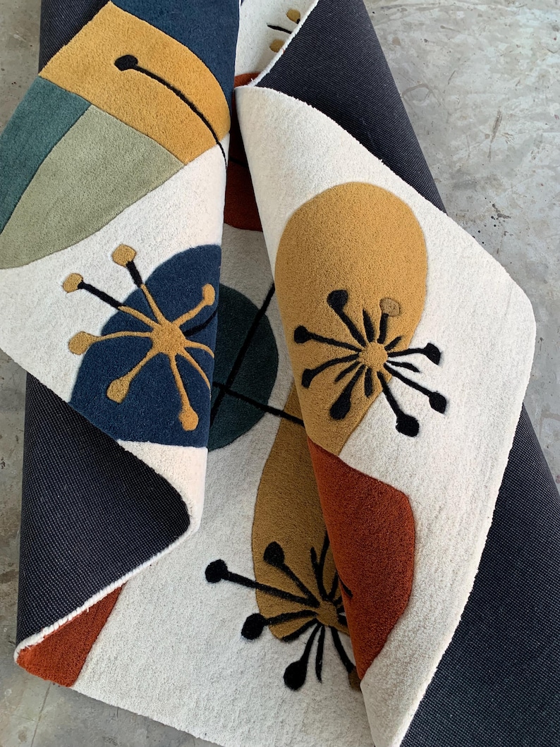 Puede incluir: Una alfombra enrollada con un dise&ntilde;o moderno de mediados de siglo. La alfombra presenta un fondo crema con formas abstractas en azul marino, amarillo mostaza, &oacute;xido y verde oliva. Tambi&eacute;n hay detalles florales negros.