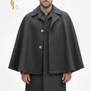 May include: A charcoal gray cape coat with a matching long coat underneath. The cape has a collar and two silver buttons. The model is wearing a green shirt. The image has a gold crown logo in the upper left corner.
