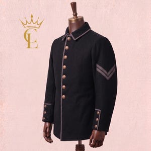May include: Black wool jacket with gray trim, gold buttons, and gray chevrons on the sleeve. The jacket is displayed on a wooden mannequin. A gold logo is in the upper left corner.