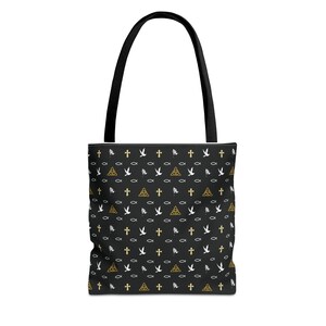 Puede incluir: Bolso tote negro con un patrón repetido de cruces doradas, palomas, peces y nudos celtas. El bolso tiene un asa negra y está diseñado para transportar objetos. El bolso está hecho de un material duradero.
