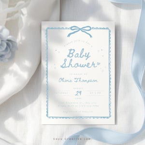 Könnte beinhalten: Babyparty-Einladung mit hellblauer Schleife und dekorativem Rand. Die Einladung enthält den Text "Baby Shower" und Details für Olivias Babyparty, einschließlich Datum und Uhrzeit. Das Design ist schlicht.