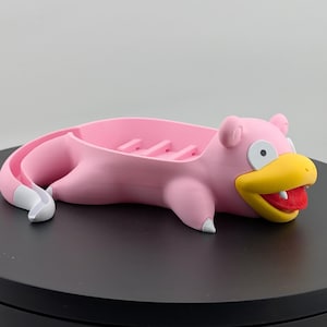 Pu&ograve; includere: Un portasapone rosa a forma di Slowpoke, con becco giallo e bocca rossa. Il portasapone ha dettagli bianchi ed &egrave; su una superficie nera. Progettato per contenere sapone.