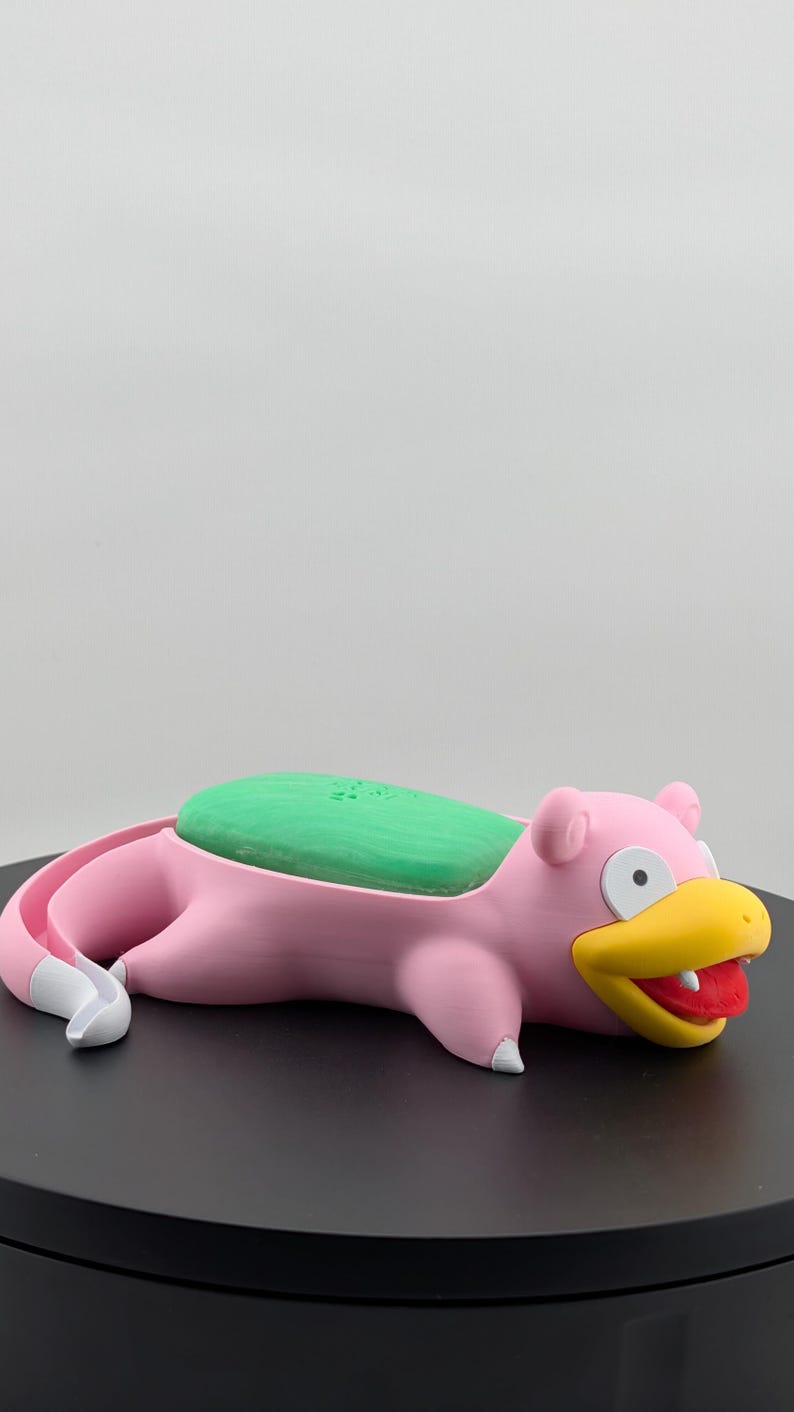 Pu&ograve; includere: Un portasapone rosa a forma di Slowpoke con una saponetta verde. Il portasapone ha un becco giallo, bocca rossa e dettagli bianchi. Il prodotto &egrave; progettato per contenere una saponetta.