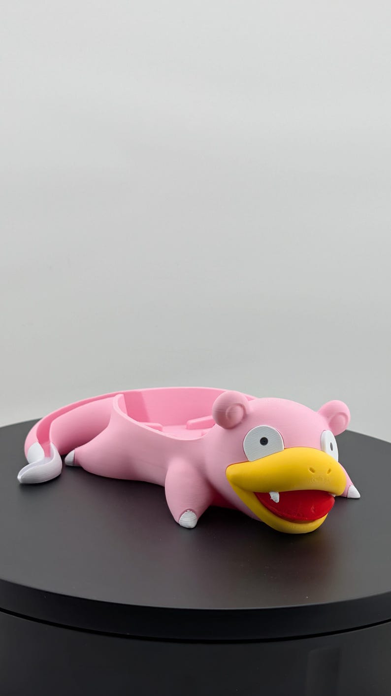 Pu&ograve; includere: Un vassoio rosa a forma di Slowpoke con dettagli bianchi su piedi e coda. Il vassoio ha un becco giallo, bocca rossa e occhi neri. Progettato per contenere piccoli oggetti, &egrave; posto su una superficie nera.