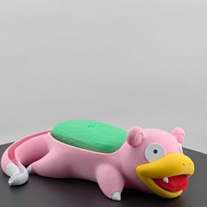 Pu&ograve; includere: Un portasapone rosa a forma di Slowpoke con sapone verde. Il portasapone ha un becco giallo, una lingua rossa e dettagli bianchi. Il prodotto &egrave; progettato per contenere una saponetta.