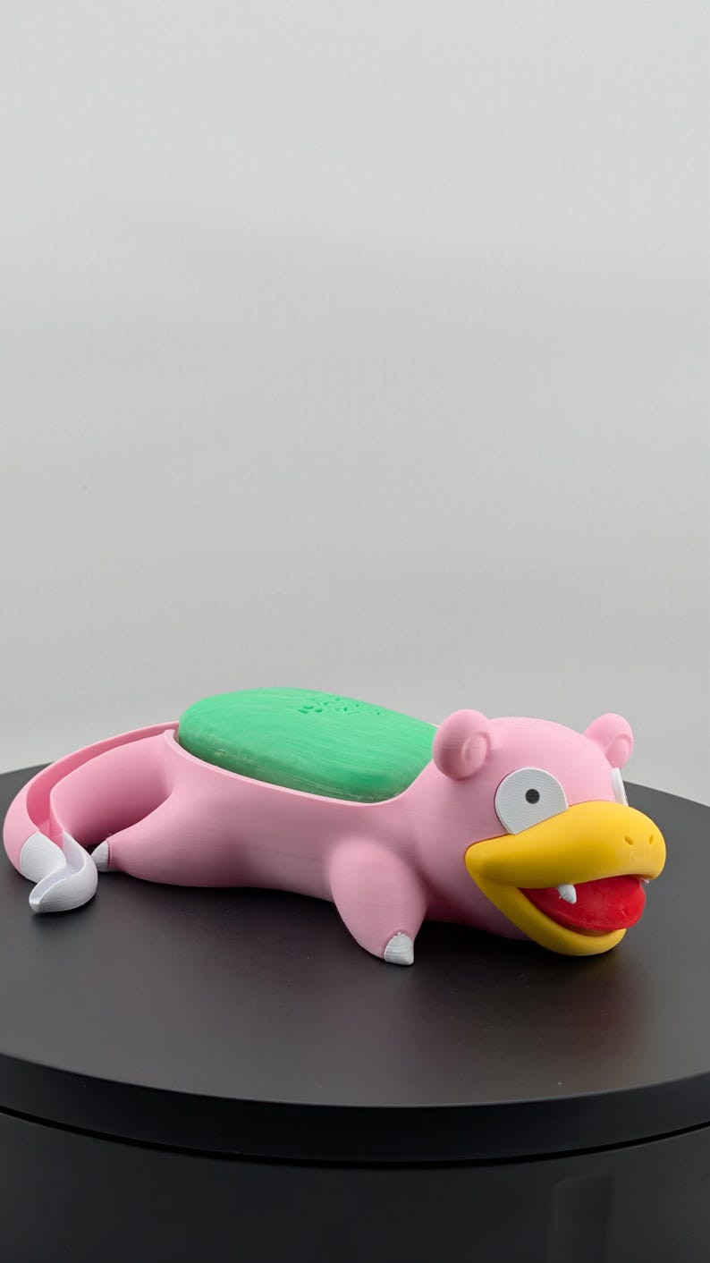 Pu&ograve; includere: Un portasapone rosa a forma di Slowpoke con sapone verde. Il portasapone ha un becco giallo, una lingua rossa e dettagli bianchi. Il prodotto &egrave; progettato per contenere una saponetta.