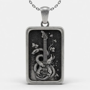May include: A rectangular silver-toned pendant necklace featuring a detailed relief carving of an electric guitar entwined with a snake and surrounded by small floral elements. The metal has a dark, oxidized finish within the recessed areas.