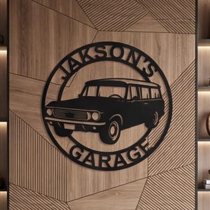 May include: Black metal sign featuring a vintage station wagon silhouette within a circle, with the text "Jakson's Garage". The sign is mounted on a wooden wall with geometric paneling, and is surrounded by decorative shelves.