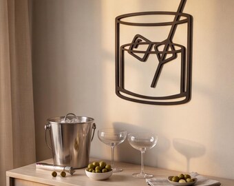 May include: A dark brown, flat, wall-mounted metal cutout depicting a stylized rocks glass filled with two ice cubes and a long stirring rod. The design features clean, bold lines that form the silhouette of a cocktail glass and its contents.