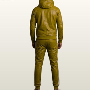 May include: An olive green leather tracksuit consisting of a hooded jacket and matching trousers. The jacket features a hood and long sleeves with ribbed cuffs. The trousers have a slim fit with white side stripes and ribbed ankles. White sneakers.