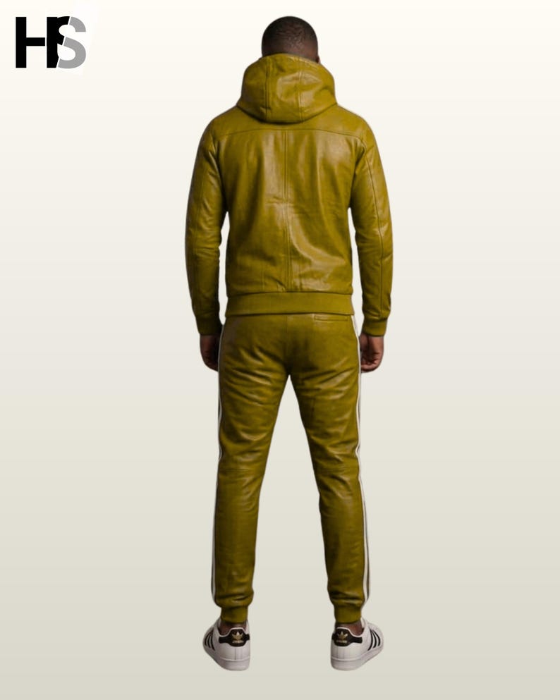 May include: An olive green leather tracksuit consisting of a hooded jacket and matching trousers. The jacket features a hood and long sleeves with ribbed cuffs. The trousers have a slim fit with white side stripes and ribbed ankles. White sneakers.