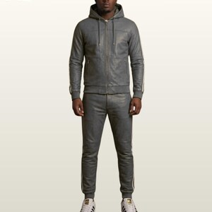May include: A grey leather tracksuit consisting of a hooded zip-up jacket with drawstrings and matching slim-fit joggers. Both pieces feature white side stripes along the sleeves and legs. The outfit is paired with white sneakers with black stripes.