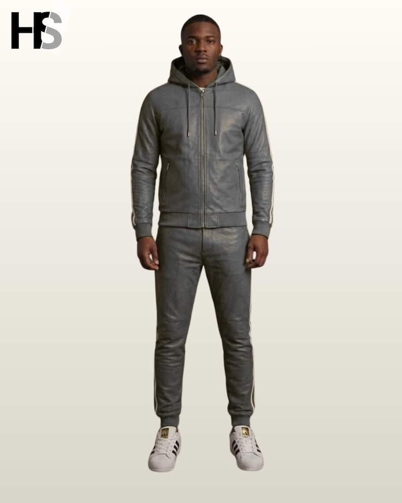 May include: A grey leather tracksuit consisting of a hooded zip-up jacket with drawstrings and matching slim-fit joggers. Both pieces feature white side stripes along the sleeves and legs. The outfit is paired with white sneakers with black stripes.