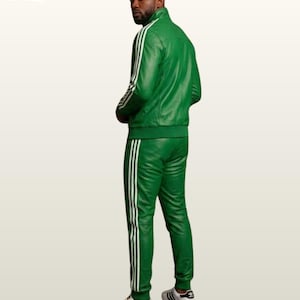 May include: A vibrant green leather tracksuit featuring a high-neck zip-up jacket and matching trousers. Both pieces are adorned with three white vertical stripes running down the sleeves and legs. The outfit is paired with white sneakers.