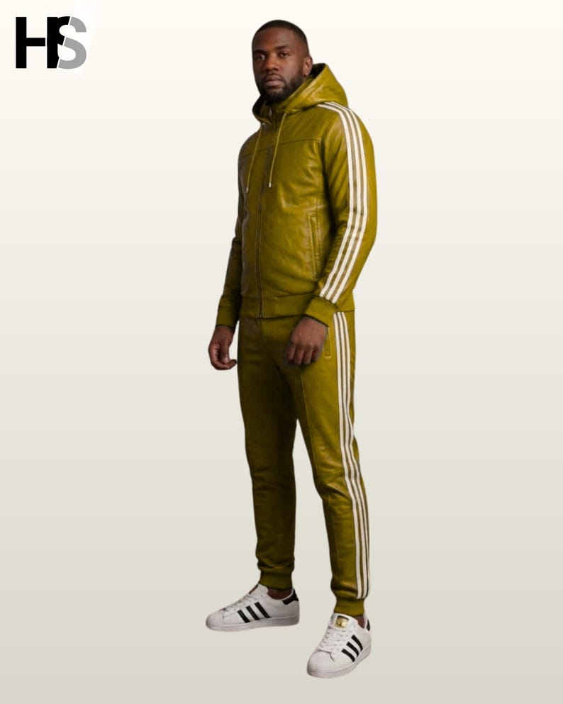 May include: An olive green leather tracksuit featuring a hooded zip-up jacket and matching joggers. Both pieces are accented with three white vertical stripes along the sleeves and legs. The outfit is paired with white sneakers with black stripes.