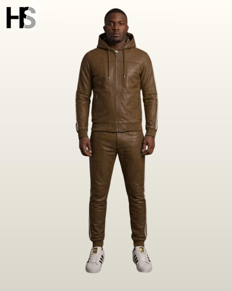 May include: A brown leather tracksuit consisting of a hooded zip-up jacket with long sleeves and matching trousers. The jacket features a front zipper, a hood with drawstrings, and side pockets. Both pieces have white side stripes and ribbed cuffs.