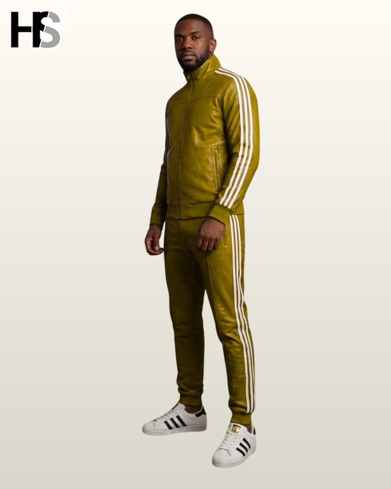 May include: An olive green track suit featuring a full-zip jacket with a high collar and matching slim-fit track pants. Both pieces are adorned with three white vertical stripes running down the sleeves and legs. The outfit is paired with white sneakers.