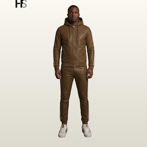 May include: A brown leather tracksuit consisting of a hooded zip-up jacket with long sleeves and matching slim-fit trousers. The jacket features a front zip, drawstrings, and side pockets. The trousers have ribbed cuffs and white side stripes.