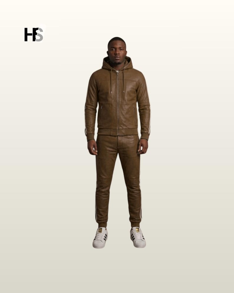 May include: A brown leather tracksuit consisting of a hooded zip-up jacket with long sleeves and matching slim-fit trousers. The jacket features a front zip, drawstrings, and side pockets. The trousers have ribbed cuffs and white side stripes.