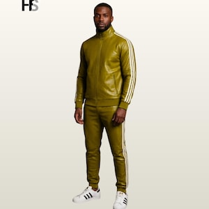 May include: An olive green track suit featuring a full-zip jacket with a high collar and matching slim-fit trousers. Both pieces are accented with three white vertical stripes along the sleeves and legs. The outfit is paired with white sneakers.