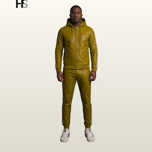 May include: An olive green leather tracksuit featuring a hooded zip-up jacket with long sleeves and matching slim-fit trousers. The set includes white side stripes running down the arms and legs. The logo HS is visible in the upper left corner.