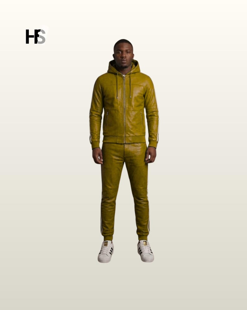 May include: An olive green leather tracksuit featuring a hooded zip-up jacket with long sleeves and matching slim-fit trousers. The set includes white side stripes running down the arms and legs. The logo HS is visible in the upper left corner.