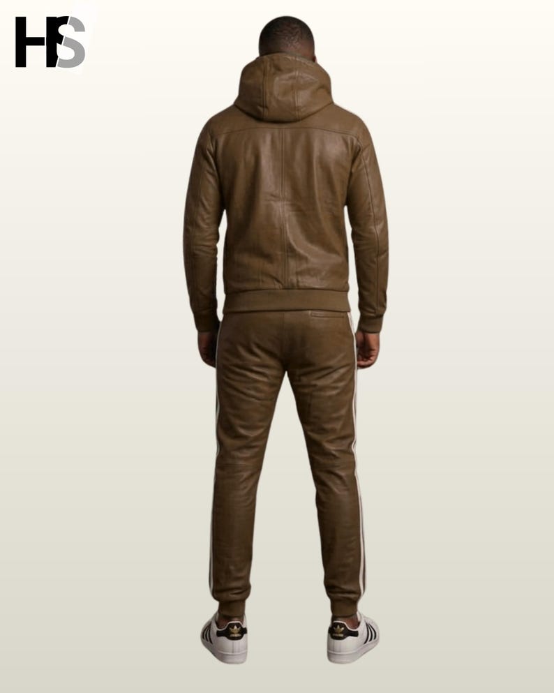May include: A brown leather tracksuit consisting of a hooded jacket and matching trousers. The jacket features a hood and long sleeves with ribbed cuffs. The trousers have a straight-leg fit with white side stripes. White trainers are worn with the set.