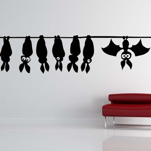 May include: A white wall with a red door and a row of black bat silhouettes hanging from a string. A red couch is in the foreground.