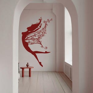 May include: A red silhouette of a dancing figure with flowing hair and decorative wing-like elements on a white wall. The image is in a room with arched doorways and a small table.