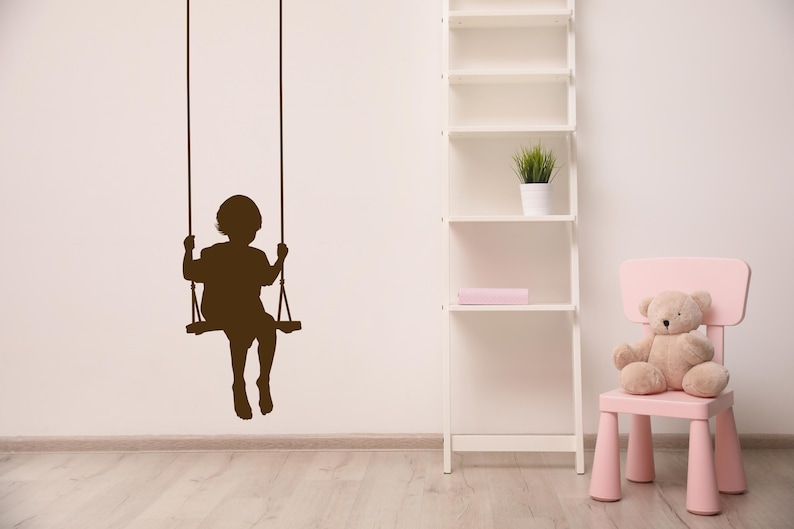 Swing wall decal featuring a child silhouette on a rope swing, designed as a renter friendly window decal that brings a nostalgic sense of childhood wonder and gentle movement. Child on a rope swing wall decal. Toddler silhouette is shown in the laundry room, playroom, nursery, bedroom, etc... Farmhouse, country, rustic decor.