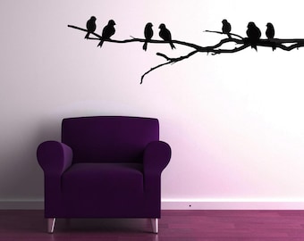 May include: A purple armchair sits in front of a white wall with a black silhouette of a branch with birds on it.