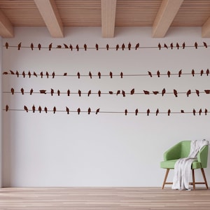 May include: A white wall with a series of black bird silhouettes on a wire, creating a decorative pattern. The wall is in a room with a wooden ceiling and a green armchair with a white throw blanket.