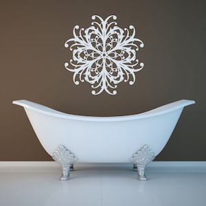 May include: A white clawfoot bathtub with silver feet sits in front of a brown wall with a white decorative floral stencil on the wall.
