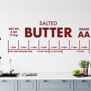 May include: A wall decal featuring a red graphic with the words "SALTED BUTTER" and "GRADE AA". It includes measurements from 1 TBSP to 8 TBSP, with net weight of 4 oz (113g). The decal is designed for kitchen use.