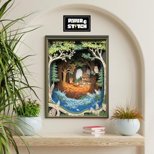 May include: A framed paper art piece showing a layered forest scene with a fox, house, and owl. The artwork uses green, brown, and blue. The text "PAPER & STITCH" is in a black box at the top.