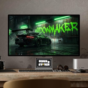 以下が含まれることがあります： コンピューターモニターには、緑色のグラフィティで「WIDOWMAKER」と書かれた黒いスポーツカーのデジタルアートが表示されています。「PAPER & STITCH」というテキストが入ったラップトップが下にあります。木製の机の上にセットアップされています。