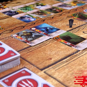 Puede incluir: Configuraci&oacute;n de un juego de mesa con cartas ilustradas y un tapete de juego con efecto de madera. Las cartas muestran im&aacute;genes y texto, con un emblema rojo y blanco en el reverso. El tapete de juego tiene gr&aacute;ficos relacionados con el juego.