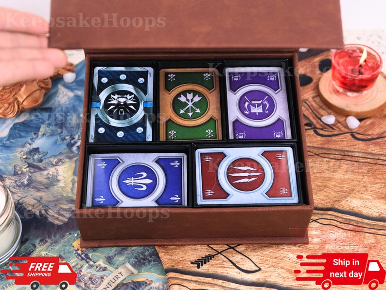 Puede incluir: Una caja de madera marr&oacute;n que contiene cinco cartas con diferentes dise&ntilde;os. Las cartas presentan varios colores, incluyendo azul, verde y rojo, con s&iacute;mbolos y emblemas. La caja est&aacute; abierta, revelando las cartas cuidadosamente dispuestas en su interior.