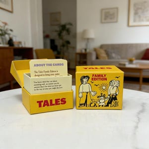 May include: A yellow box game titled "TALES FAMILY EDITION" with illustrations of people and text. The box is open, revealing a stack of cards with text. The game is designed to bring your entire family together.