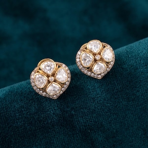 May include: A pair of gold stud earrings, each featuring four pear-shaped clear stones arranged in a flower-like cluster. The base of each earring is accented with a border of tiny pavé-set stones, creating a rounded, heart-inspired silhouette.