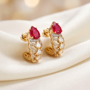 May include: A pair of gold hoop earrings featuring a prominent pear-shaped red gemstone at the top, accented by a series of smaller, clear, teardrop-shaped stones and pavé-set diamonds arranged in an intricate, openwork lattice design.