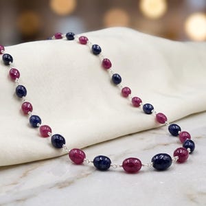May include: A necklace featuring alternating oval-shaped beads in deep blue and vibrant pinkish-red hues. The smooth, polished stones are connected by thin silver-toned metal links, creating a delicate chain that follows a repeating color pattern.