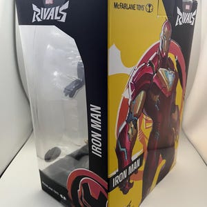 Może przedstawiać: Pudełko z figurką Iron Man z serii Marvel Rivals od McFarlane Toys. Opakowanie posiada przezroczyste plastikowe okienko z przodu, ż&oacute;łty panel boczny z ilustracją Iron Mana w kolorach czerwonym i złotym oraz nadrukowany tekst Marvel Rivals i Iron Man.