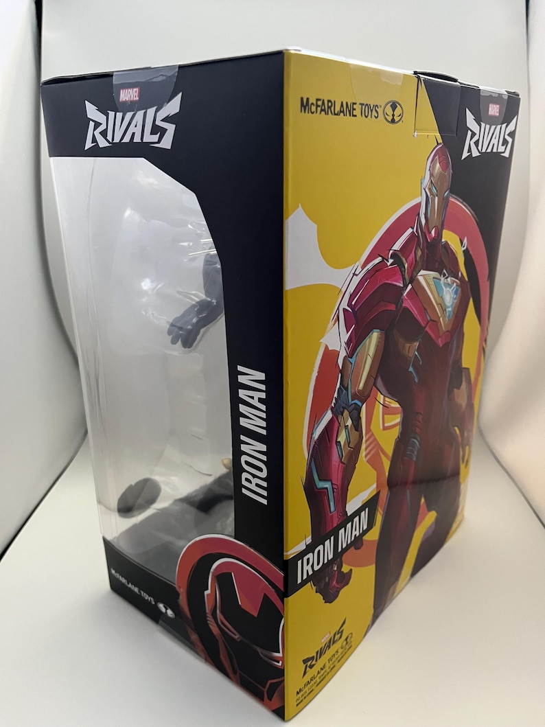 Może przedstawiać: Pudełko z figurką Iron Man z serii Marvel Rivals od McFarlane Toys. Opakowanie posiada przezroczyste plastikowe okienko z przodu, ż&oacute;łty panel boczny z ilustracją Iron Mana w kolorach czerwonym i złotym oraz nadrukowany tekst Marvel Rivals i Iron Man.
