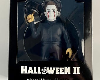 May include: A boxed Michael Myers vinyl figure from Halloween II. The figure is in a black box with the text "HALLOWEEN II" and "Michael Myers - Vinyl Figure". The figure is wearing a dark blue jumpsuit and a white mask with red blood streaks.