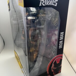 Może przedstawiać: Figurka akcji Iron Man z serii Marvel Rivals w oryginalnym opakowaniu. Czarne pudełko zawiera logo Marvel Rivals, napis Iron Man oraz grafikę hełmu postaci. Logo McFarlane Toys jest widoczne w dolnej części opakowania.