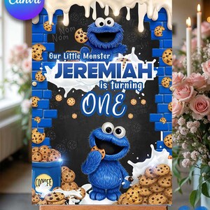 Könnte beinhalten: Personalisierte Geburtstafel mit dem blauen Cookie Monster-Charakter, der einen Keks hält. Auf der Tafel steht "Our Little Monster Jeremiah is turning ONE" mit Keks- und Milchspritzgrafiken. Die Tafel wird auf einer hölzernen Staffelei präsentiert.