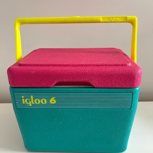 Op de afbeelding: Een vintage Igloo 6 koelbox met een getextureerde teal basis en een getextureerde roze deksel. De koelbox heeft een felgele handgreep en het Igloo-logo in geel. De koelbox is ontworpen om items koud te houden.